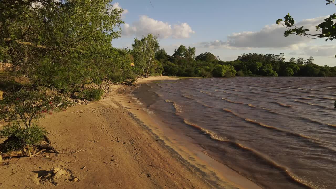 drone volando hacia atrás a baja altura entre árboles en la playa de fray bentos en uruguay