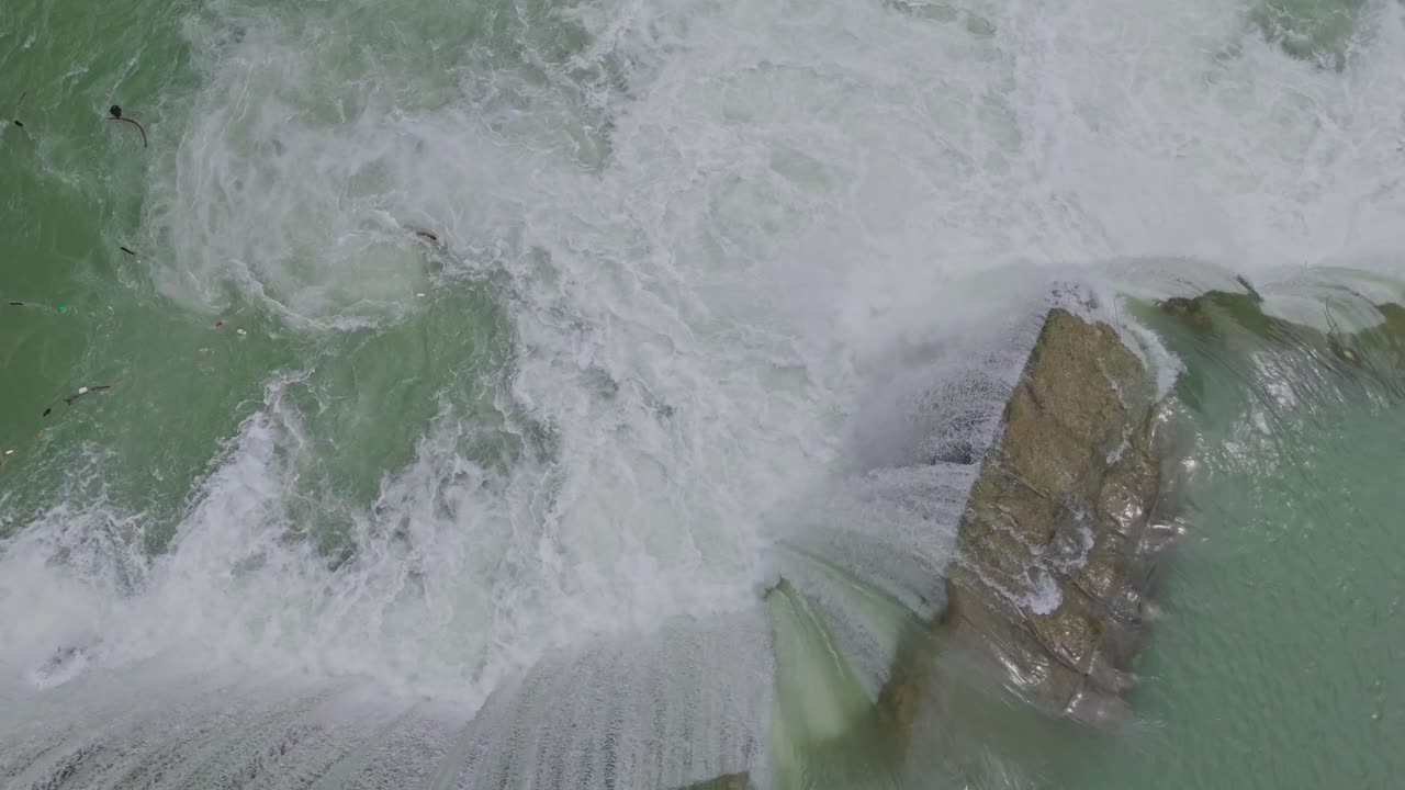 Aerial drone view of a beautiful waterfall merging into a flowing river, capturing the natural beauty of water movement, rocky terrain, and pristine landscape