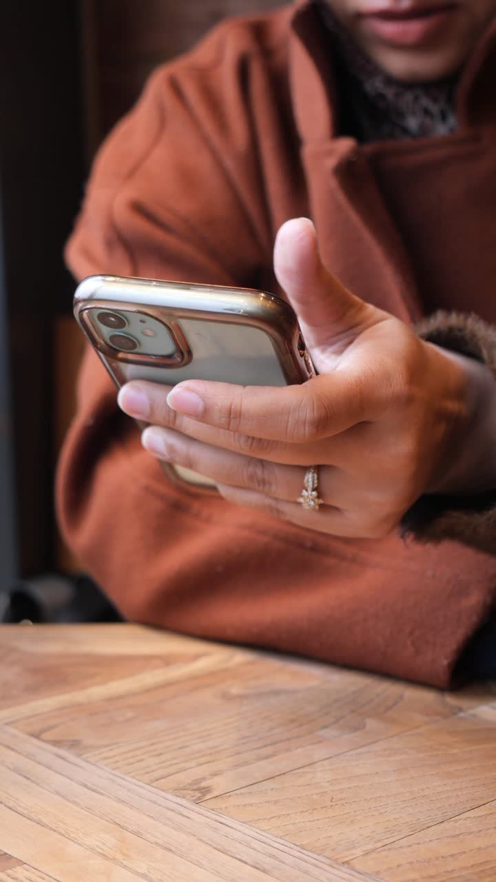 Close-up of Person's Hands Scrolling on a Smartphone at a Wooden Table