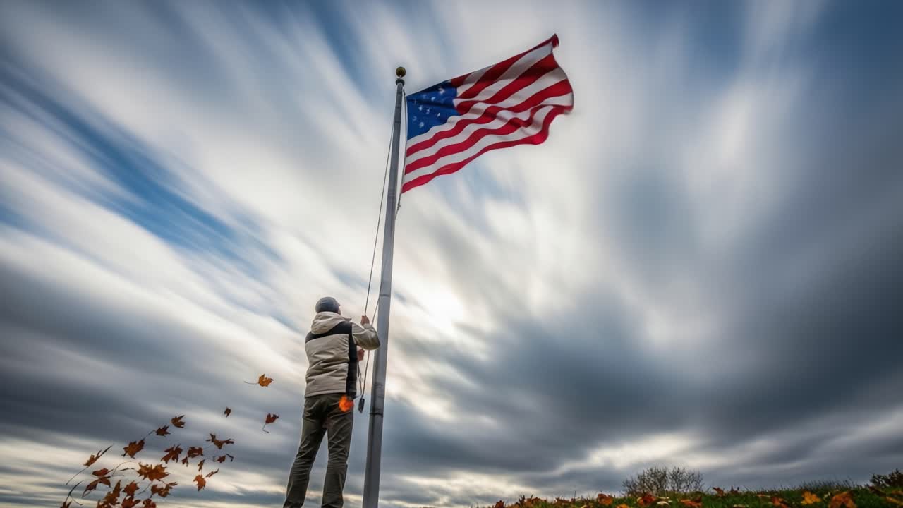 A lone individual stands beneath a majestic flagpole as the vibrant American flag billows against a dynamic sky, showcasing a moment of reflection and patriotism amidst swirling autumn leaves