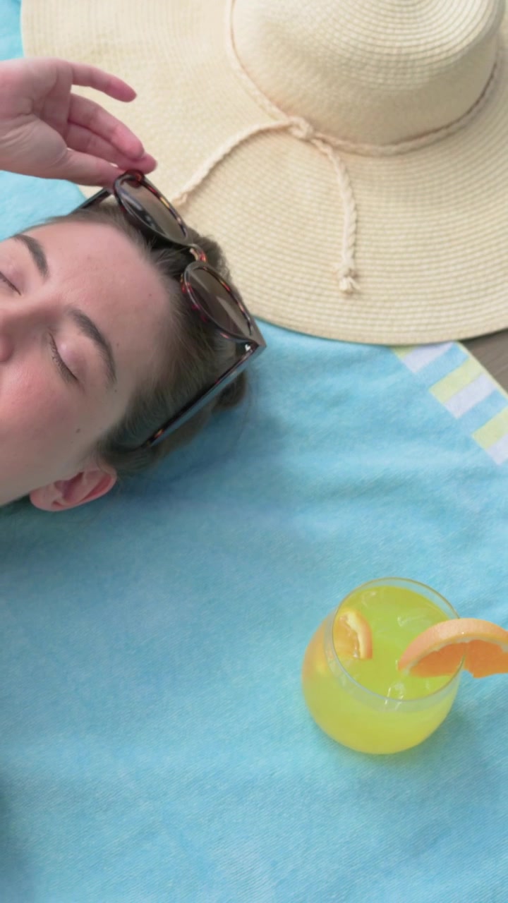 Vertical video: Camera panning woman in coral bikini, lifting sunglasses while sunbathing at pool