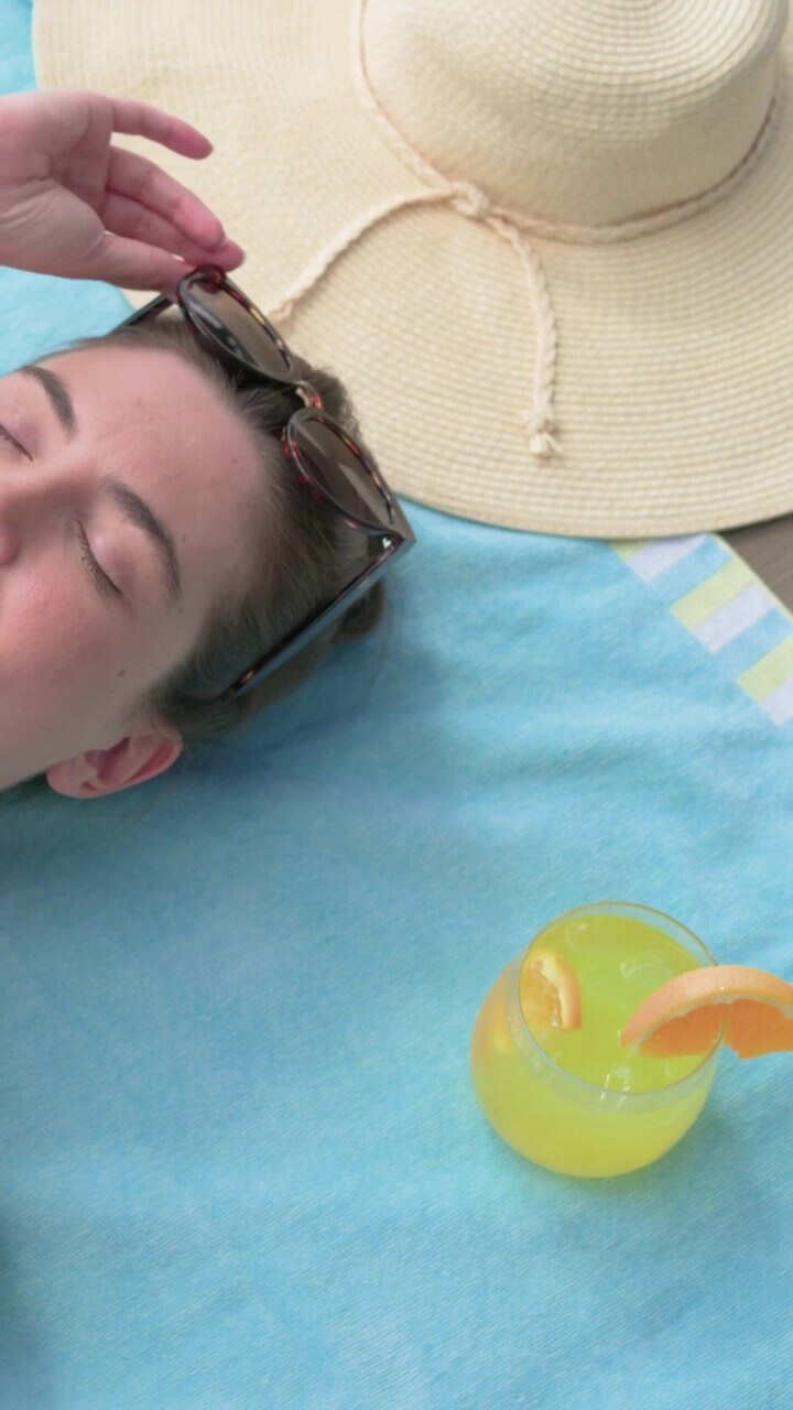 Vertical video: Camera panning woman in coral bikini, lifting sunglasses while sunbathing at pool