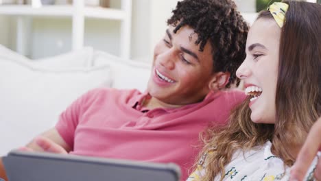 pareja biracial feliz pasando tiempo en casa juntos usando computadora portátil y teléfono inteligente