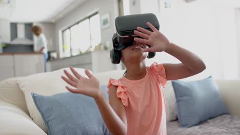 una chica biracial feliz usando auriculares vr usando una interfaz virtual en la sala de estar, en cámara lenta