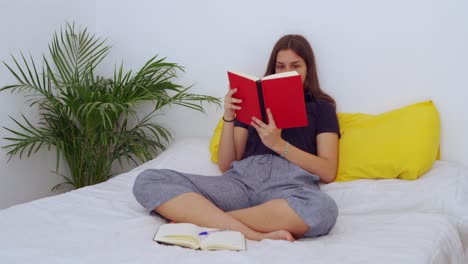 Mujer-Joven-Sentada-En-La-Cama-Y-Leyendo-Un-Libro.