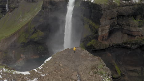 antena: un hombre vestido con una chaqueta amarilla, caminando cerca del borde de un acantilado hacia la cascada de haifoss en islandia