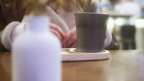 close-up of hand in brown shearling jacket gently lifting cup of coffee at cozy cafe table. soft lighting creates warm atmosphere, capturing peaceful moment of relaxation and comfort in cafe