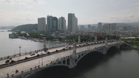 Upward-panning-drone-footage-of-traffic-along-Xing-Sheng-Bridge-in-Dali-City,-Yunnan,-China