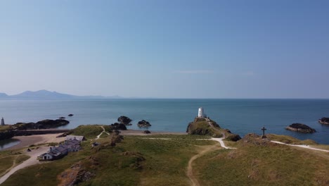 aerial view above ynys llanddwyn coastal walking trail towards goleudy tŵr mawr stone lighthouse and misty snowdonia mountains, anglesey
