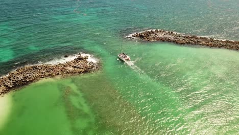 catamaran sailing between two small islands leaving a wake behind