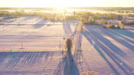 sunshine glow over small rural town during snowfall, fly away drone view