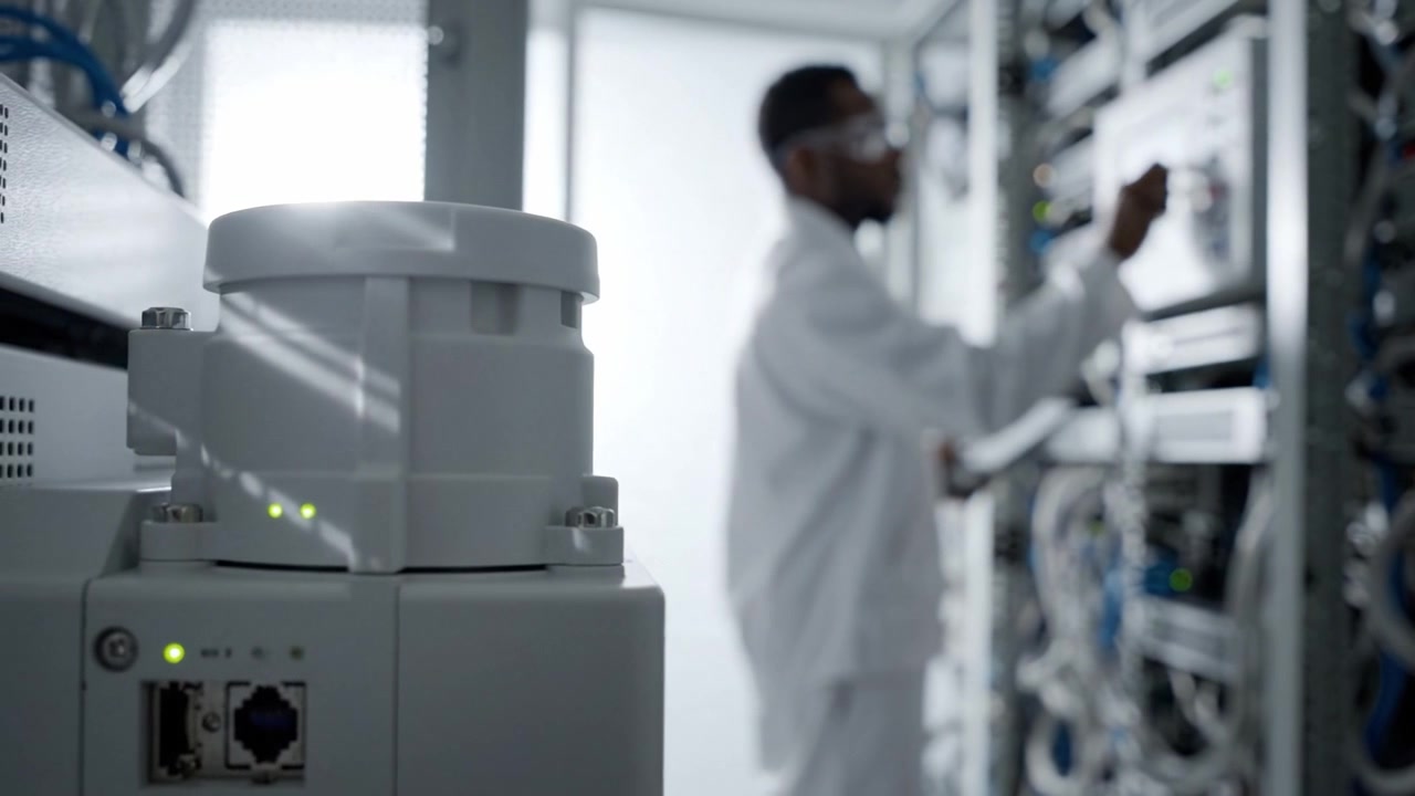 A technician in a lab coat operates a device while examining data from the network equipment within a secure server room, highlighting technology and monitoring.