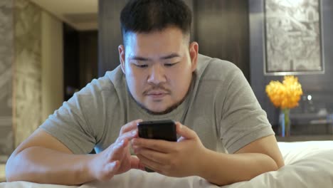 asian man while using chatting on mobile phone and lay on the bed in bed room