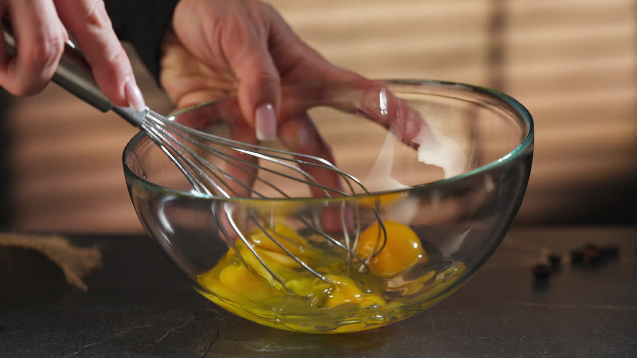 Woman beating eggs in a glass bowl with a hand mixer. Slow motion