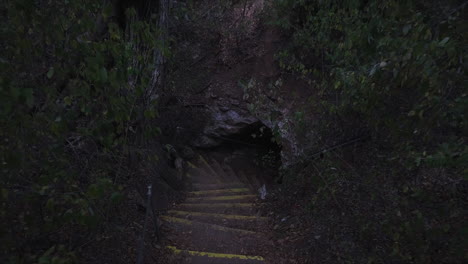 Ascending-drone-shot-of-stairs-coming-out-of-a-small-cave-opening