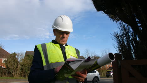 portrait of an architect senior building construction manager on a residential street with traffic and houses looking at paperwork inspecting the building