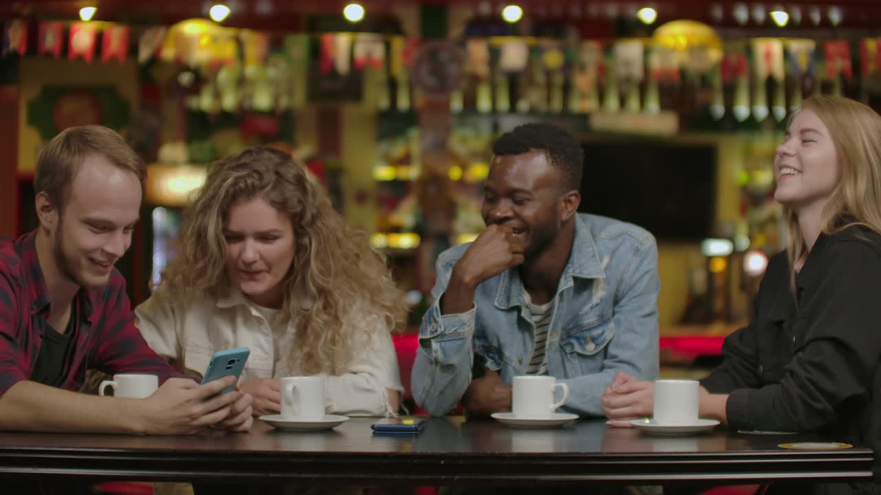 Happy multi-ethnic group of friends talking using smartphones at. Happy multi ethnic group of friends talking using smartphones in cafe diverse young people