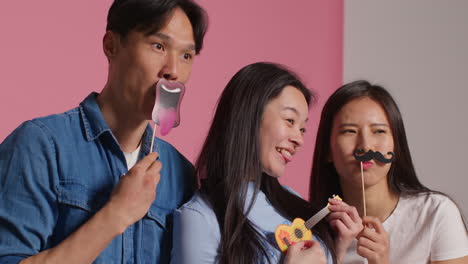 Group-Of-Young-Friends-In-Front-Of-Pink-Studio-Background-Having-Fun-Posing-For-Photo-Booth-Style-Portraits-With-Props-1