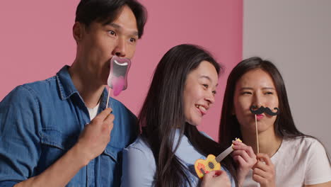 핑크색 스튜디오 배경 앞에 있는 젊은 친구 그룹이 장비로 사진 부스 스타일의 초상화를 위해 포즈를 취하고 있습니다.