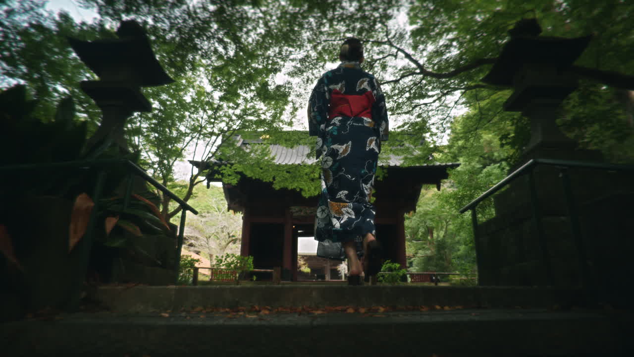 Donna in kimono che sale le scale di pietra in un giardino di un tempio