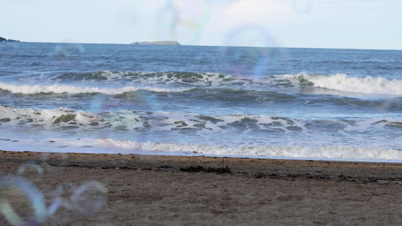 Gentle waves and floating bubbles create a serene coastal scene at Charlesworth Bay Beach, captured in soft natural light