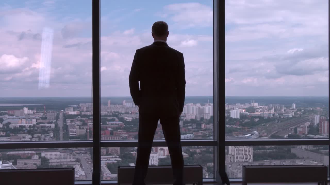 un hombre de negocios contemplando el paisaje de la ciudad desde una ventana de gran altura.