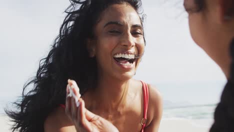 madre hispana feliz aplicando crema solar en la cara de su hija en la playa