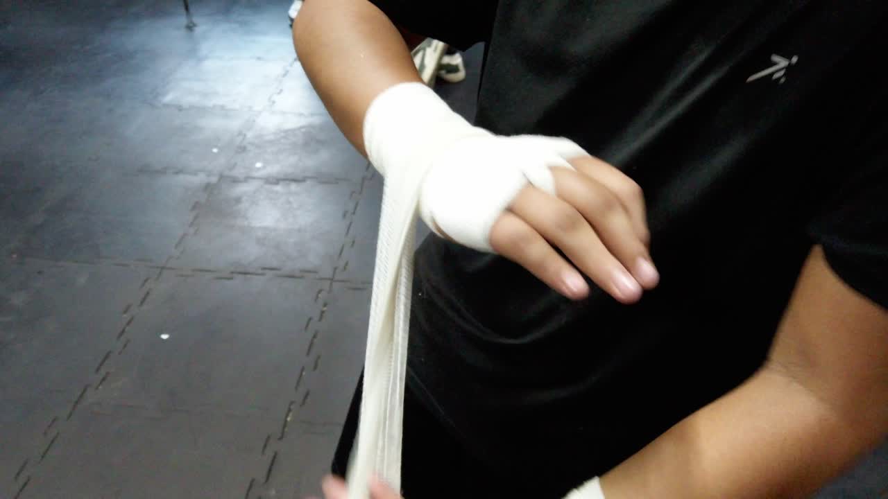 Nahaufnahme eines Athleten, der nach einer Trainingseinheit im Fitnessstudio Boxbandagen entfernt, mit Details der Hände und der Bandage.