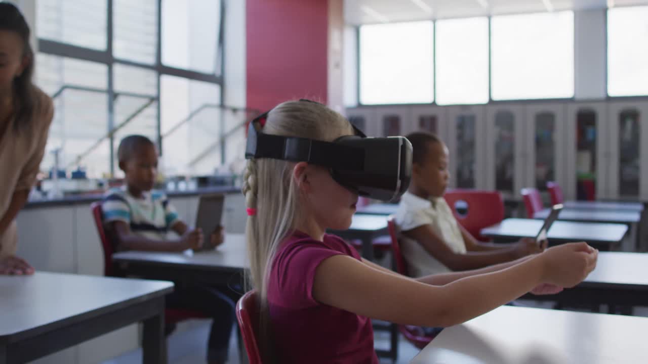 escolar caucásica sentada en el escritorio en el aula con gafas de realidad virtual y gesticulando