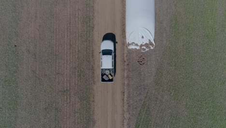 Vista-Aérea-De-Una-Camioneta-4x4-Conduciendo-A-Través-De-Un-Campo-De-Cultivo-De-Trigo-Con-Bolsas-De-Silos-En-La-Carretera