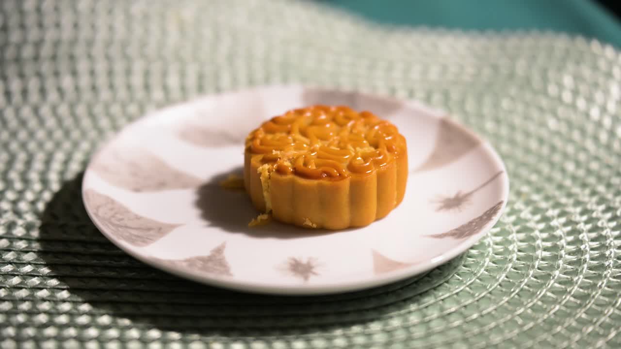 A single Chinese mooncake, featuring a decorative and intricate pattern, is presented on a plate. This traditional pastry, a symbol of the Mid-Autumn Festival, is prepared to be sliced and served