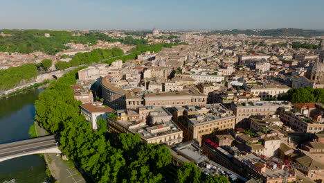 Forwards-fly-above-Tiber-river-bending-in-city.-Tilt-up-reveal-of-historic-buildings-in-city-centre.-St.-Peters-Basilica-with-large-dome-in-distance.-Rome,-Italy