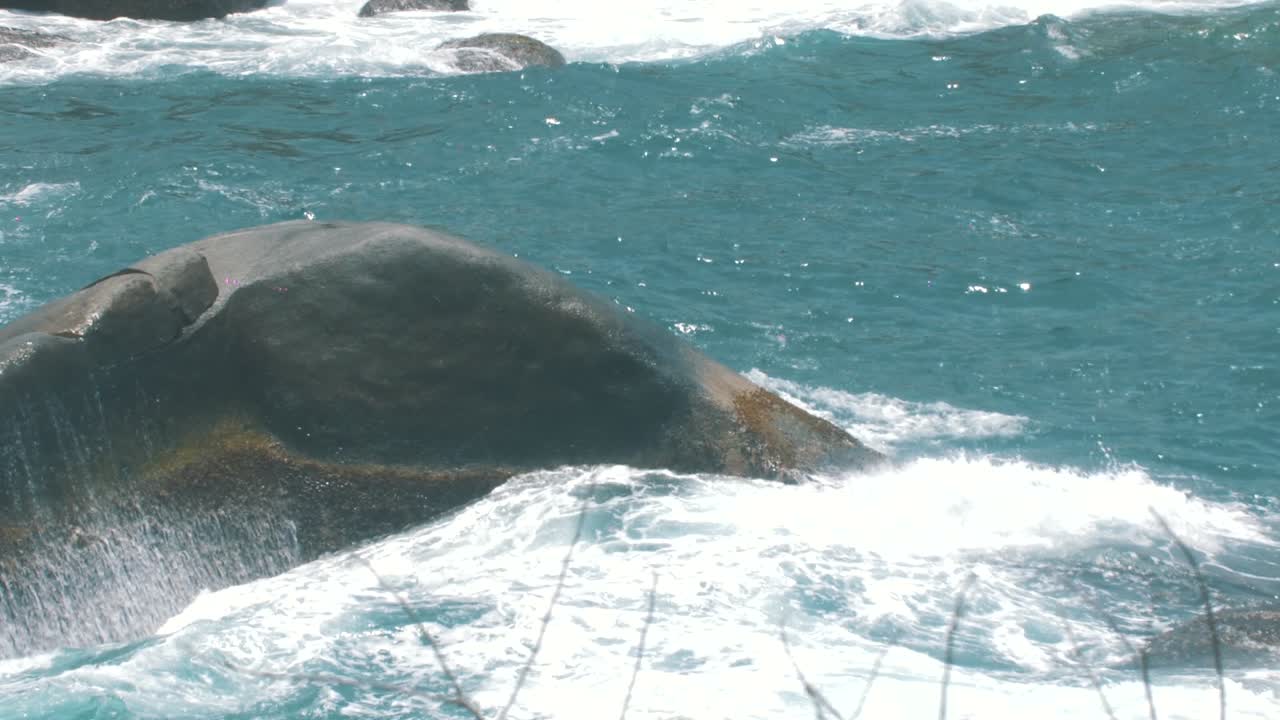 foamy waves of the blue water crashing on a rock on the sea in slow-motion - Tayrona park, colombia