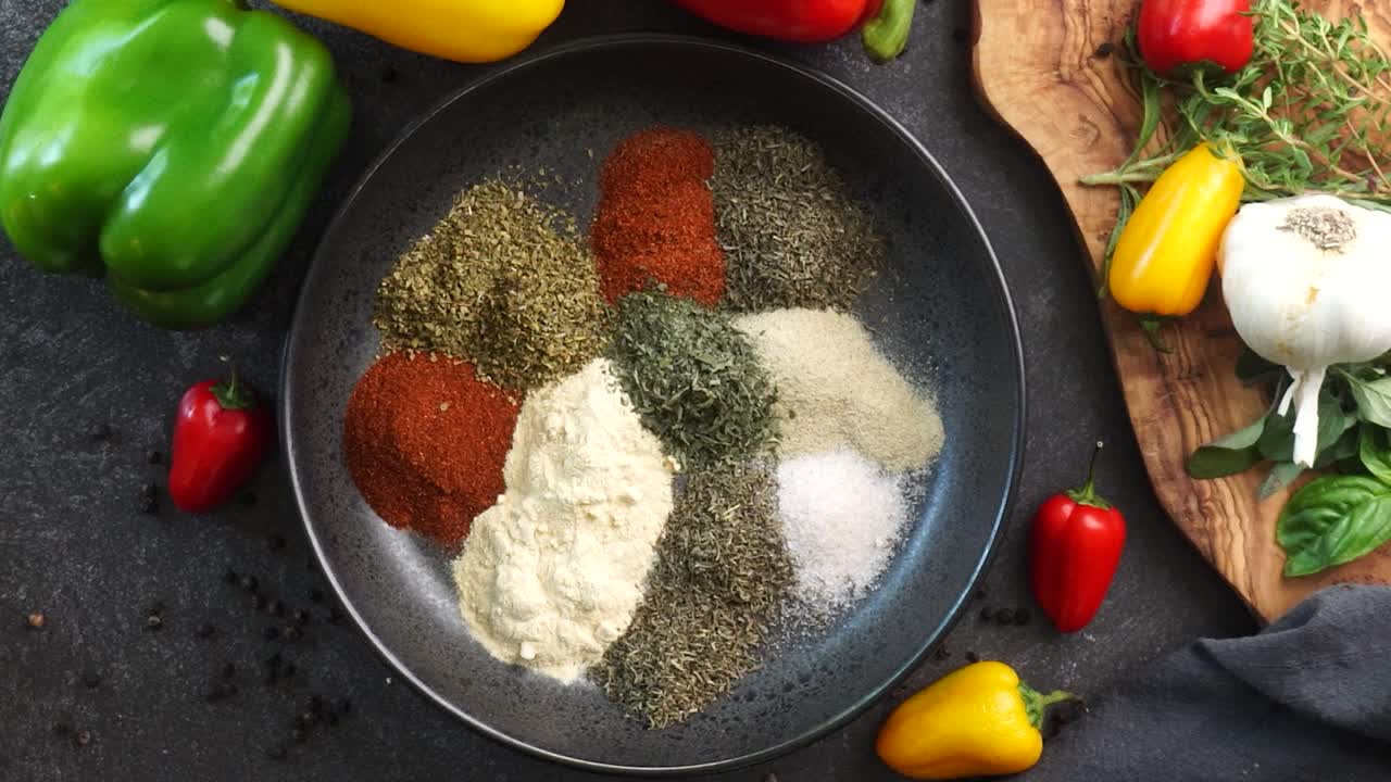 Making a vibrant Cajun Spice Blend, mixing red paprika, cayenne pepper, oregano, thyme, white garlic onion powder and black pepper in a bowl, creating a striking contrast against a black background.
