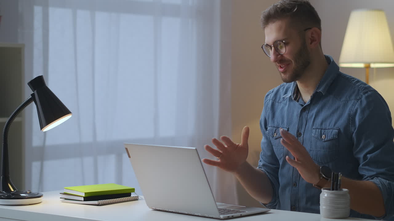 uomo gioioso sta salutando amici o colleghi tramite video call in laptop comunicazione internet con l'utilizzo di tecnologia internet seduto a tavola in casa