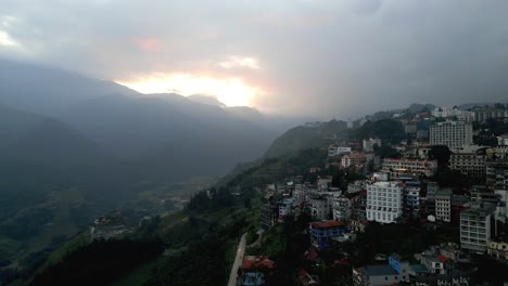 Impresionante-Antena-De-La-Ciudad-De-Una-Ciudad-En-Las-Impresionantes-Montañas-Del-Bosque-Asiático-Durante-Una-Puesta-De-Sol-En-El-Cielo-Nublado