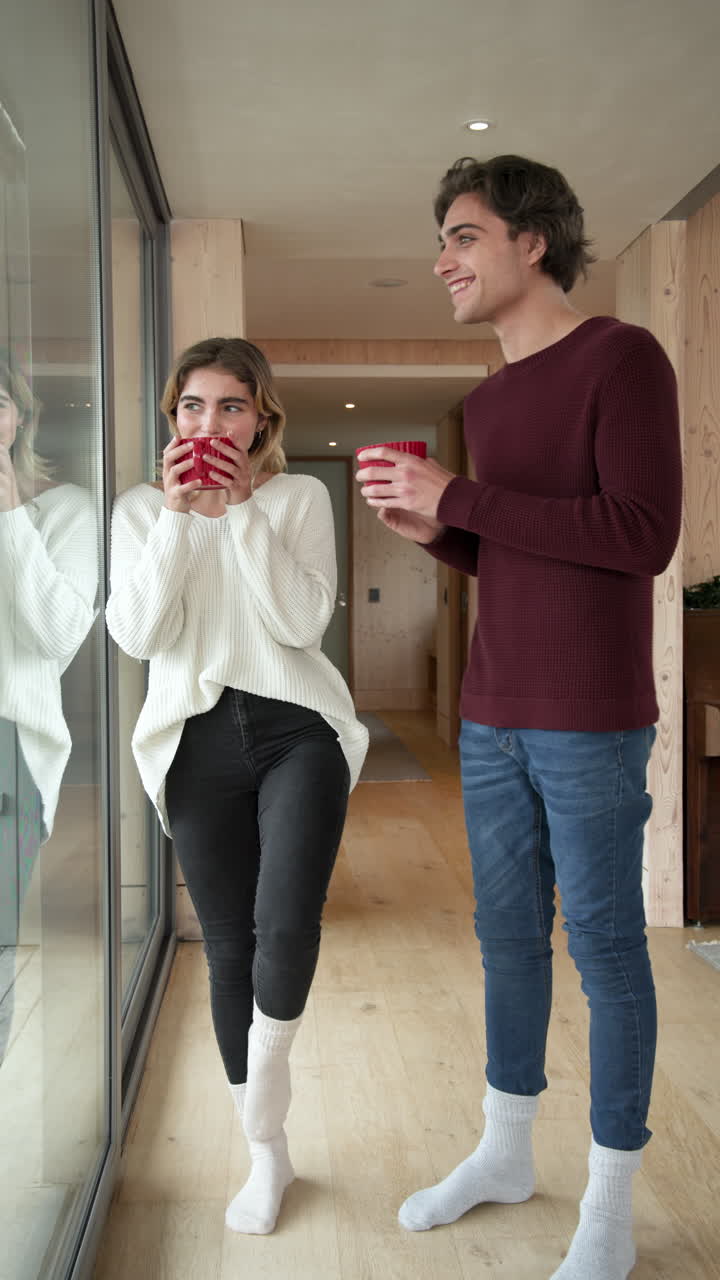 Vertical video: Couple enjoying hot drinks by window, cozy at home in winter