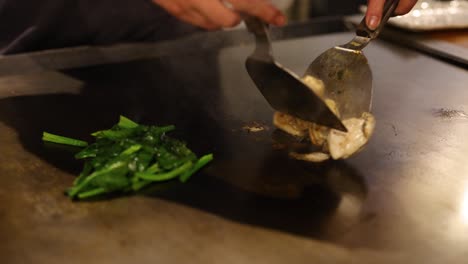 chef stir-frying oysters and greens on a hot griddle