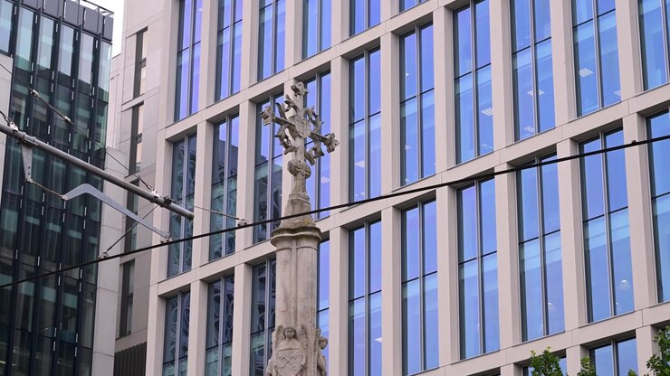 La Croce di San Pietro si erge di fronte a edifici per uffici in vetro e pietra con i cavi del tram che attraversano l'inquadratura nel centro di Manchester