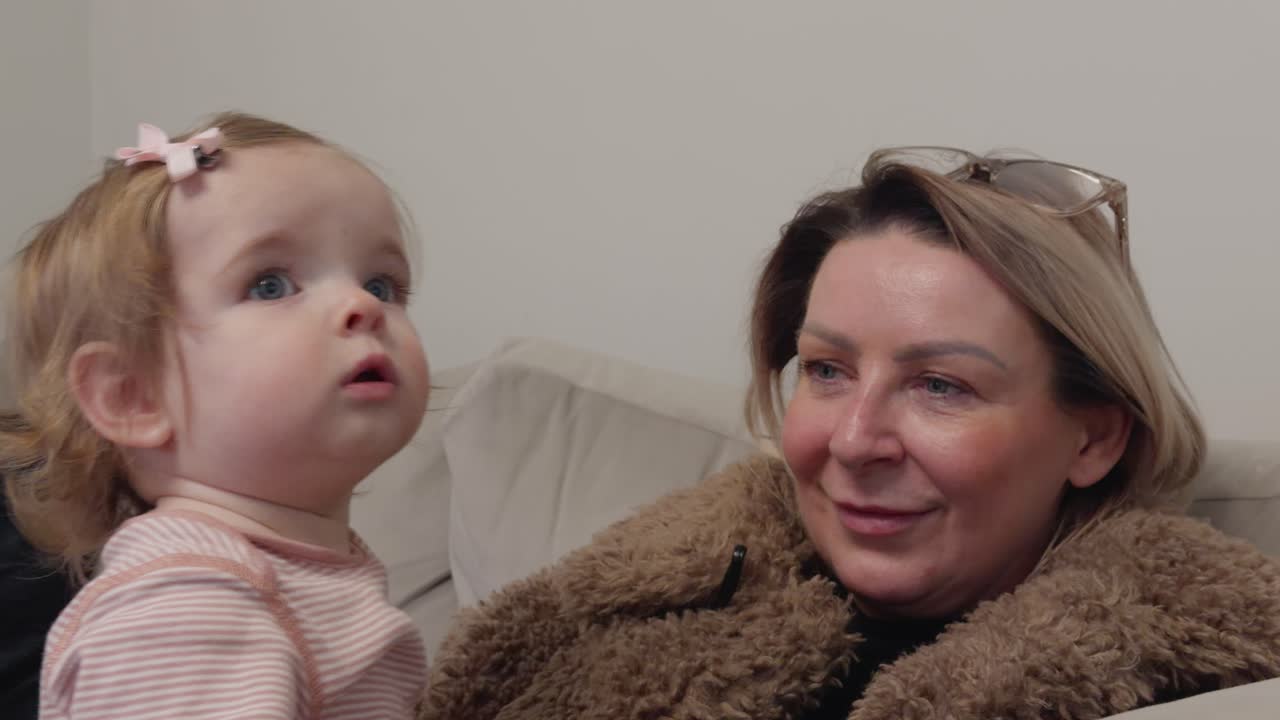 Eine Großmutter und ihre Enkelin sitzen gemeinsam auf einem Sofa in Schottland und schauen gebannt fern in einer gemütlichen häuslichen Umgebung.