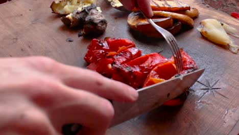 Schneiden-Von-Gerösteten-Roten-Paprika,-Mit-Geröstetem-Gemüse-Im-Hintergrund