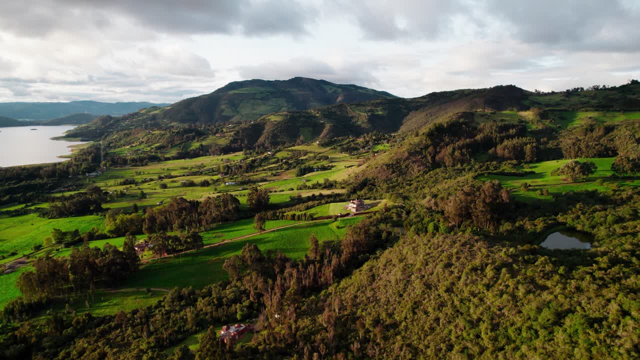 Drone descending shot over lush green mountains and fields near Guatavita, Colombia, during golden hour with warm light