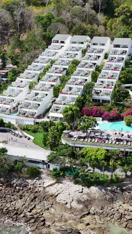 drone footage captures a scenic beachfront resort in phuket, thailand, showcasing lush greenery, clear waters, and vibrant architecture