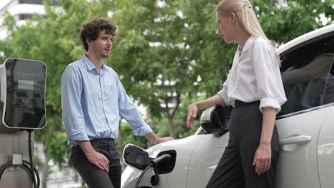 progressive businessman and businesswoman use charging station for ev car.