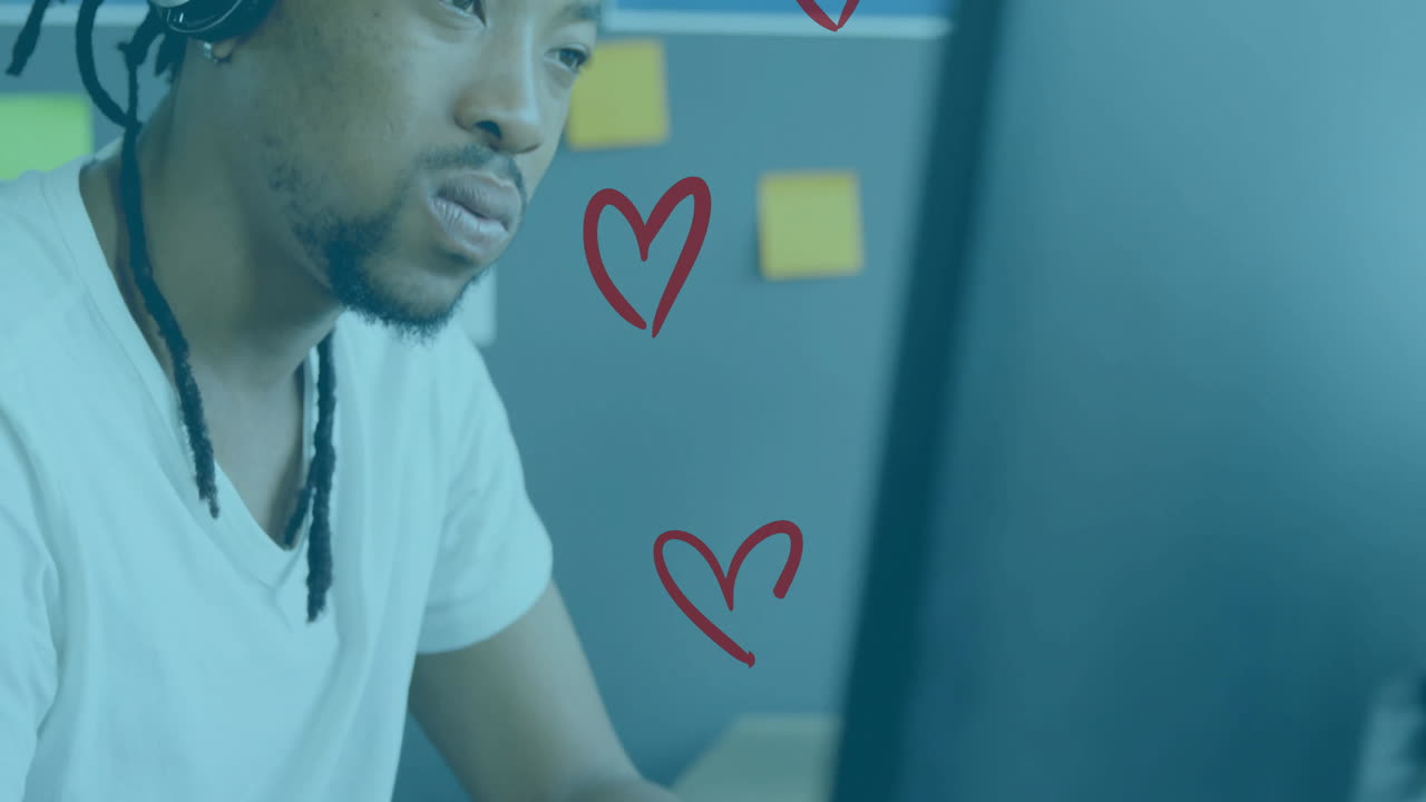 dreadlocked man wearing headphones focusing on computer for tech design, showing heart icons