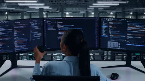 vista trasera de una desarrolladora asiática bebiendo café y usando una computadora para escribir código con múltiples pantallas en un centro de datos