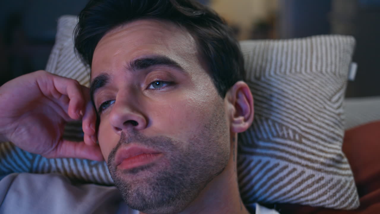 Sleepy man looking television at dark apartment closeup. TV viewer rubbing eyes