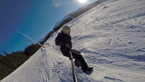 vista frontal de un snowboarder bajando a alta velocidad y saltando a cámara lenta en un día despejado con el sol detrás