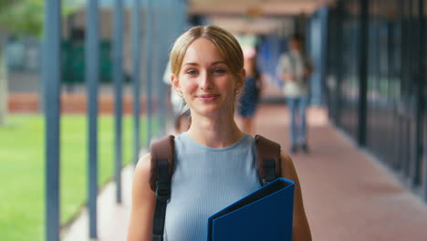 Portrait-Of-Smiling-Female-High-School-Or-Secondary-Student-With-Backpack-Outside-Classroom