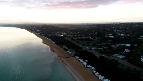 drone high overlooking coastline beach boxes and blue bay at sunrise boom up